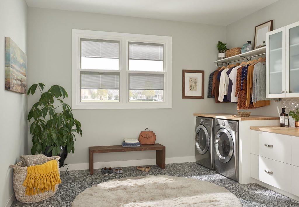 A set of white double hung windows with blinds inside of a laundry room.