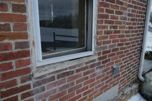 An exterior window on the side of an aged brick home.