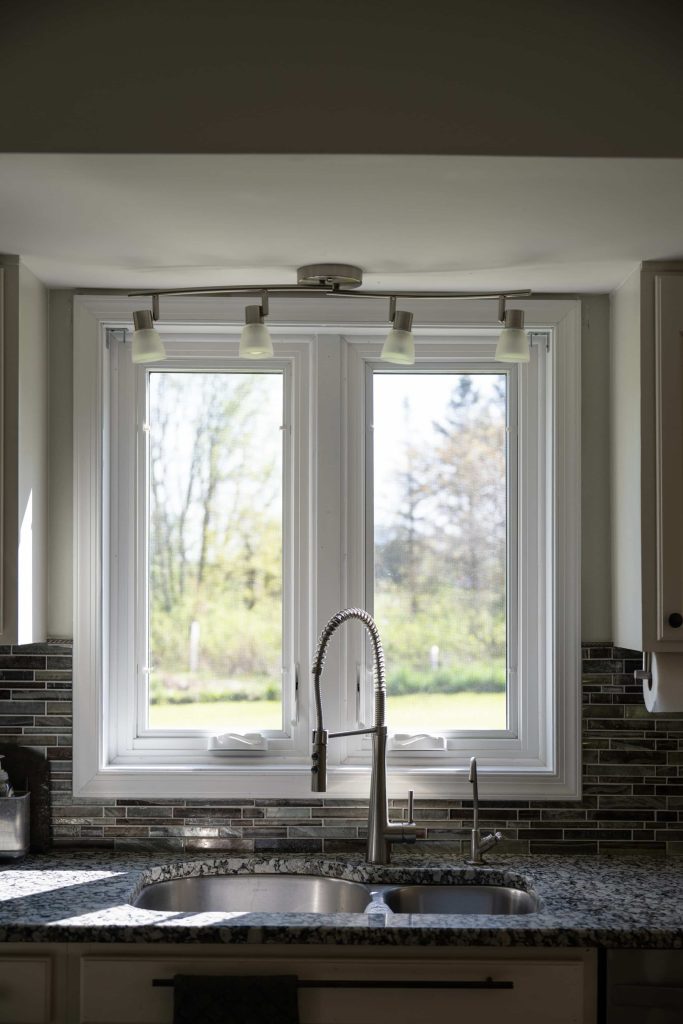 Two casement windows in a kitchen overlooking a yard.