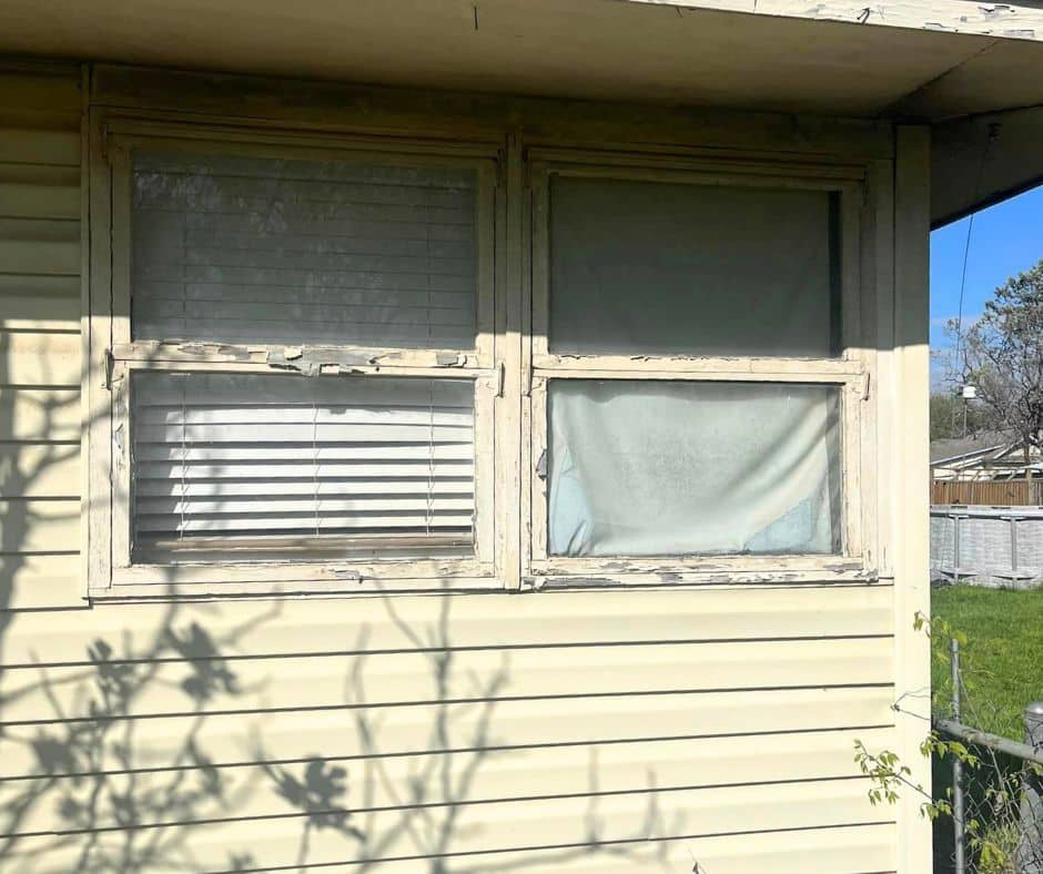 Old drafty cracked windows on the side of a tan house.