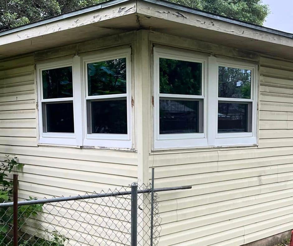 Outside view of new white double hung windows on the corner of a tan house.