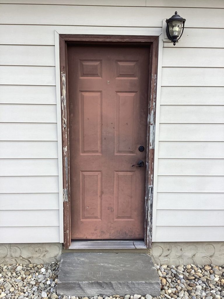 An old faded red door with chipped paint and dirt around the frame.