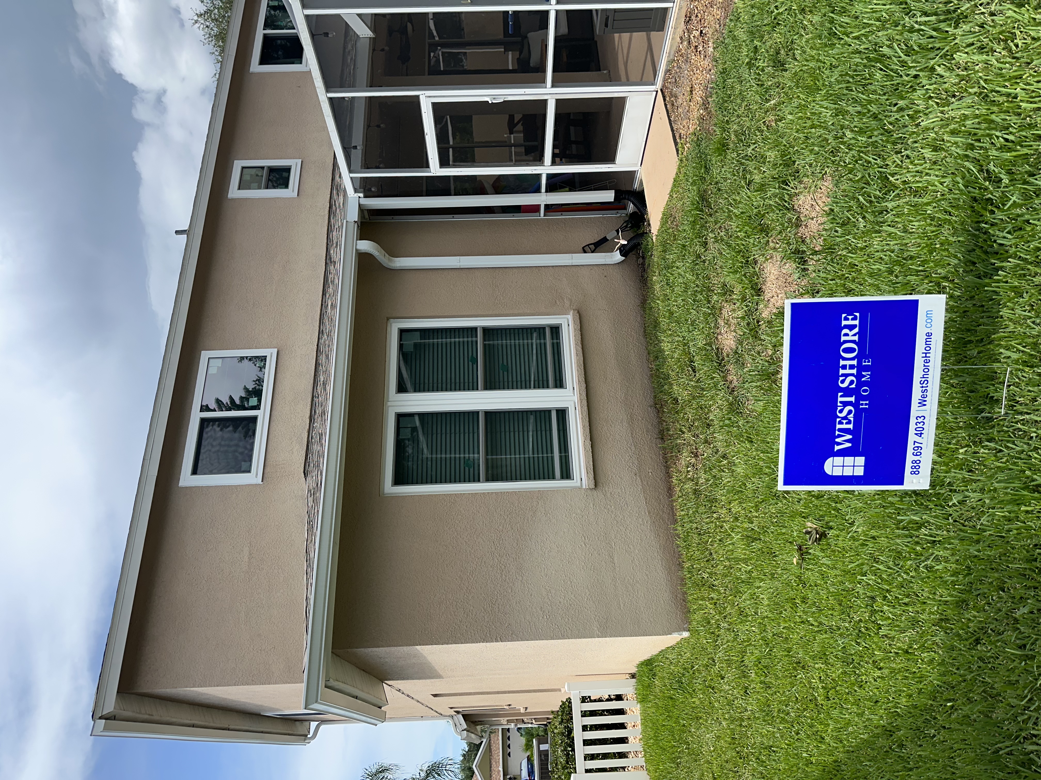 Backside of a Florida home with new white windows and a West Shore Home yard sign.