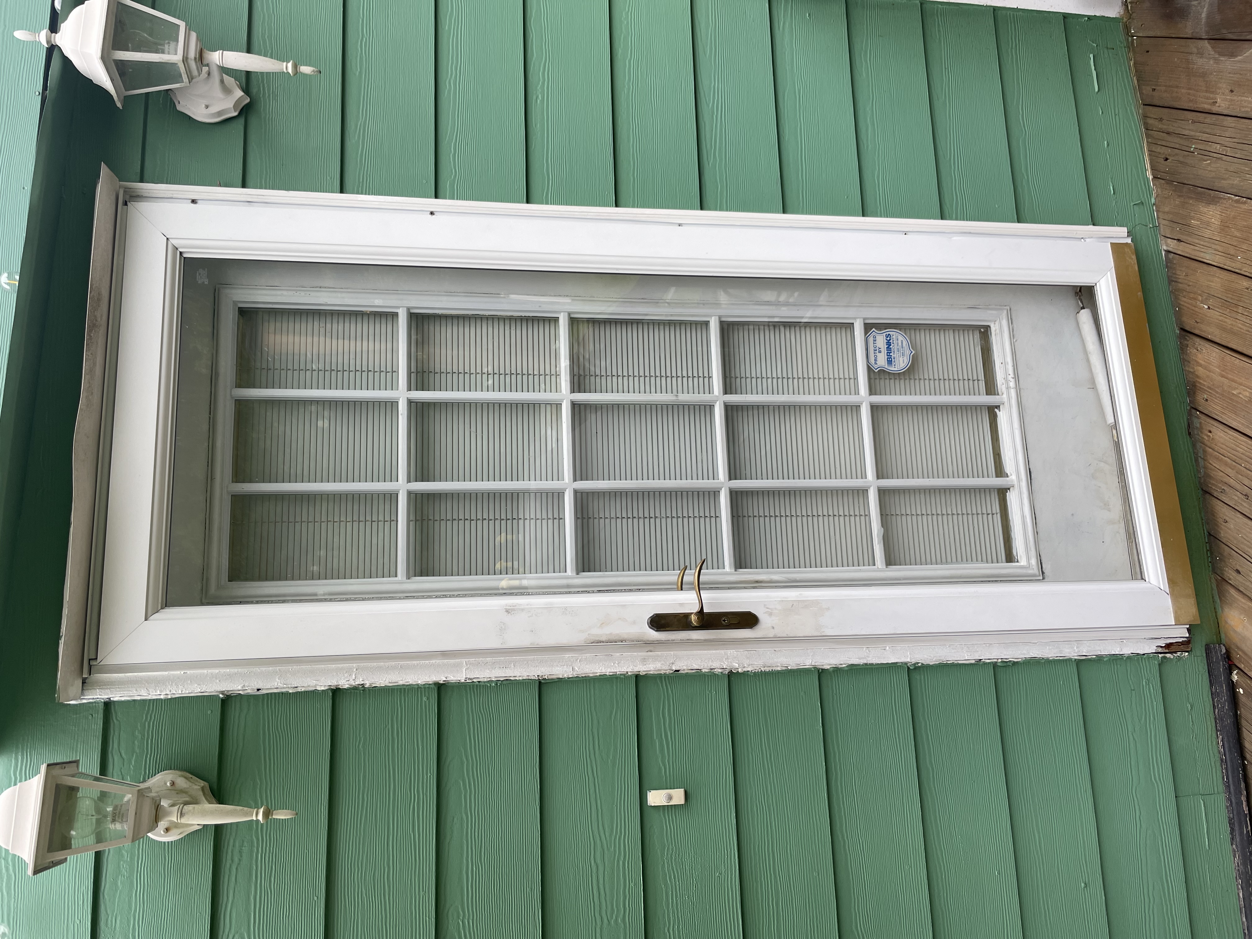 An old white door in need of a replacement on a green house. 