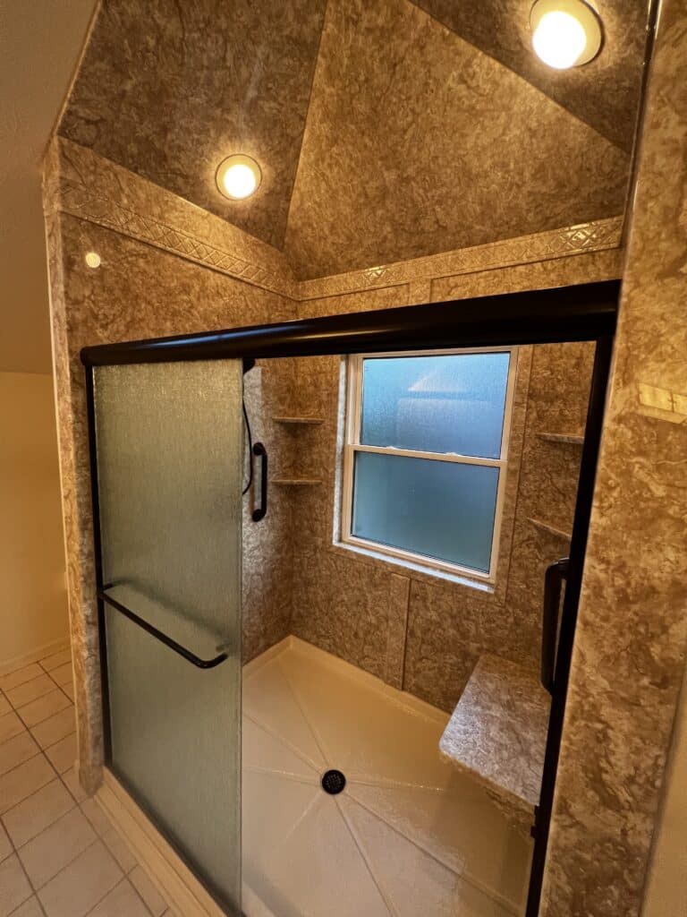 A walk in shower with glass doors, a shower seat, and black fixtures.