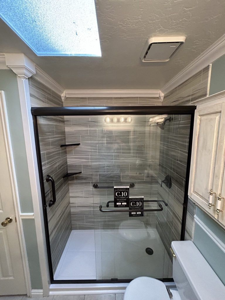 An acrylic walk in shower with grab bars, shower shelves, and sliding glass doors.