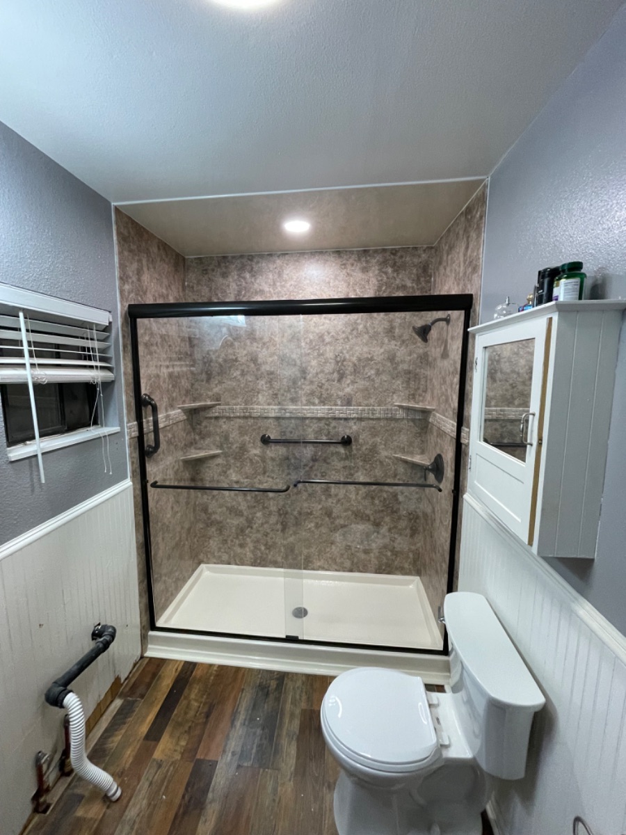 A remodeled walk in shower with granite look acrylic wall surrounds and bronze fixtures.