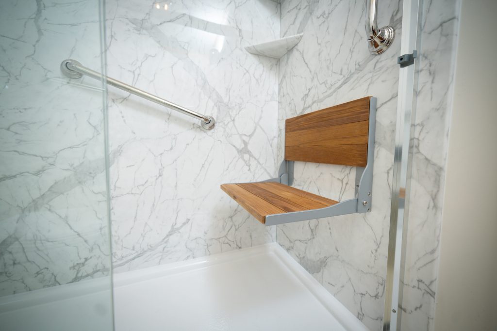 A marble acrylic walk in shower with teak shower seat and shower grab bars.