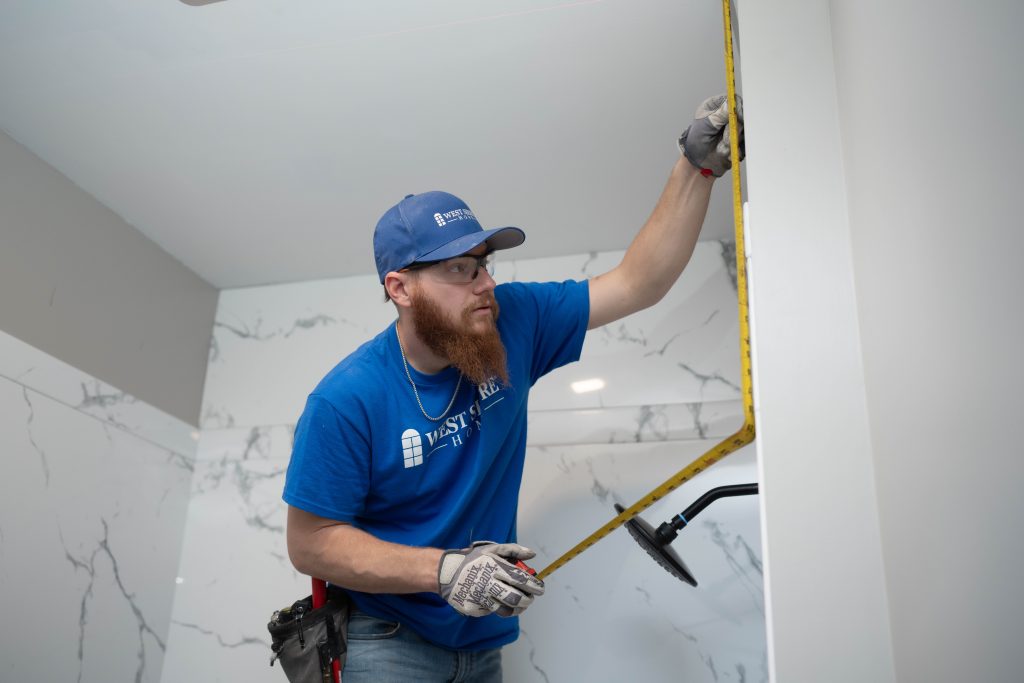 A man measuring the acrylic wall surrounds of a new shower.