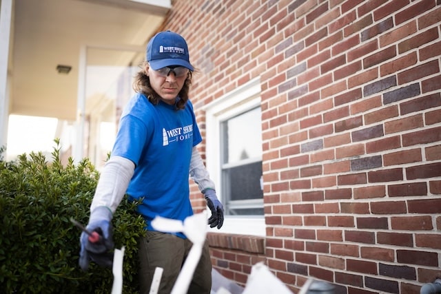 A window installer outside of a brick home working on installing a new double hung window.