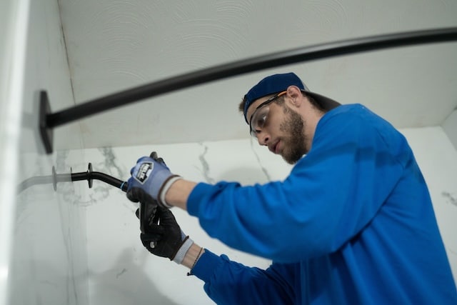 A photo of a bathroom installer installing a black showerhead in a marble acrylic shower.